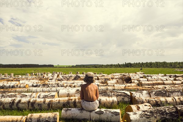 Mari boy sitting on log in rural field