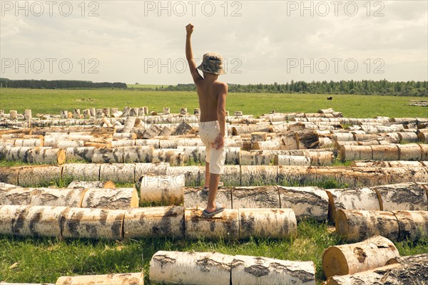 Mari boy standing on logs in rural field