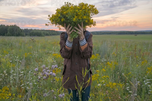 Caucasian woman holding bouquet of flowers over face in field at sunset