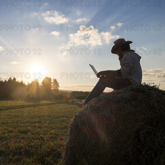 Mari man sitting on hay bale at sunset using laptop