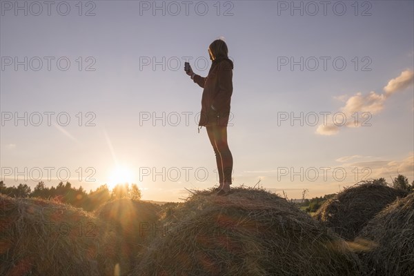 Caucasian woman standing on hay holding cell phone