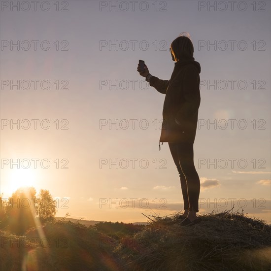 Caucasian woman standing on hay holding cell phone