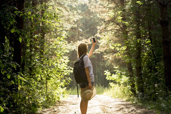 Caucasian woman photographing forest trees with cell phone