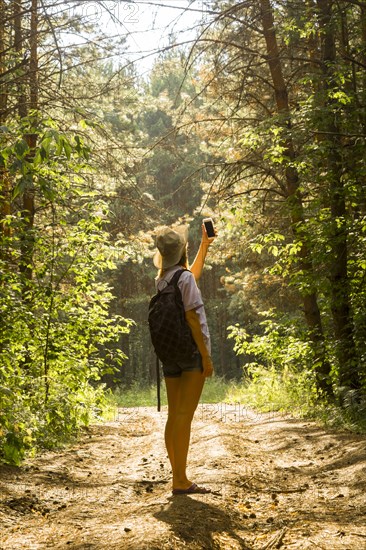 Caucasian woman photographing forest trees with cell phone