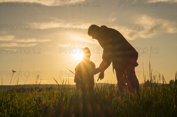 Woman and son standing in field at sunset