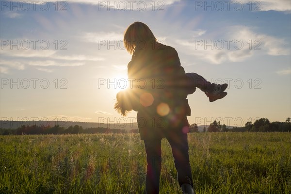 Woman carrying son in field at sunset