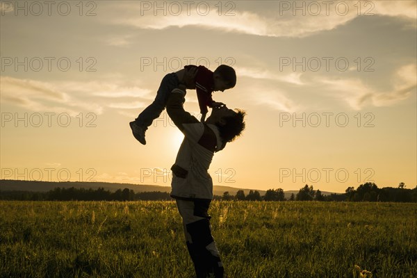 Mari man lifting son in field at sunset