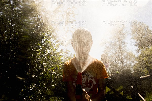 Back lit Mari boy spraying hose at face