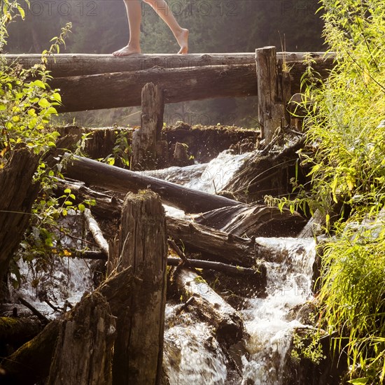 Legs of Caucasian woman walking on log crossing waterfalls
