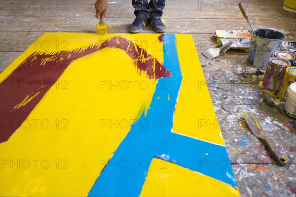 Legs of Mari man painting canvas on floor