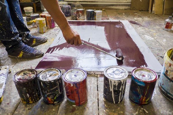 Legs of Mari man painting canvas on floor