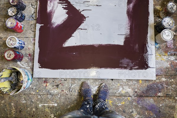 Legs of Mari man standing near paint cans and canvas on floor