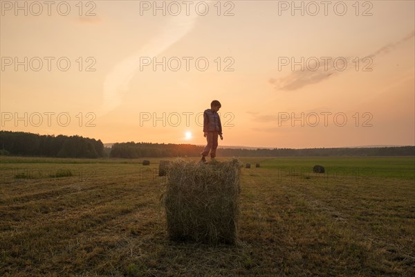 Mari boy standing on hay bale in field