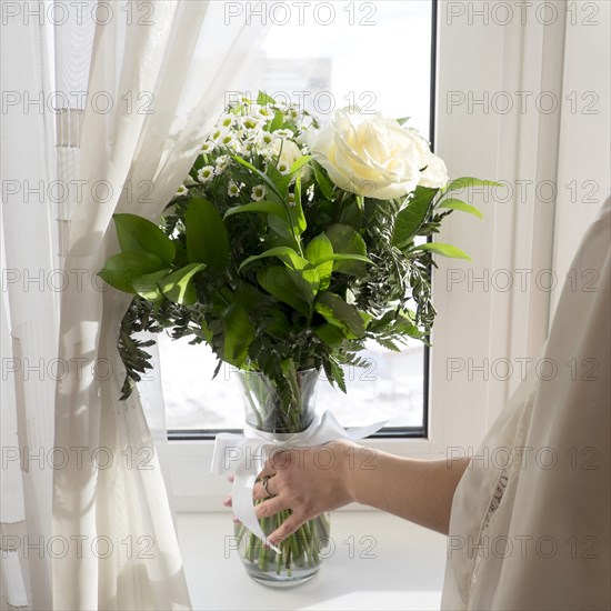 Caucasian woman placing vase of flowers on window sill