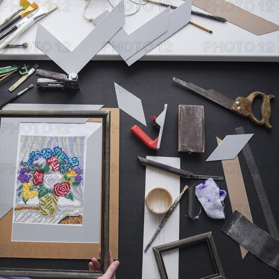 Hand holding picture frame near tools on table