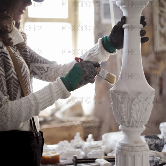 Caucasian artist using paintbrush on sculpture