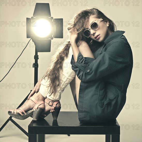 Retro Caucasian girl sitting on table near spotlight