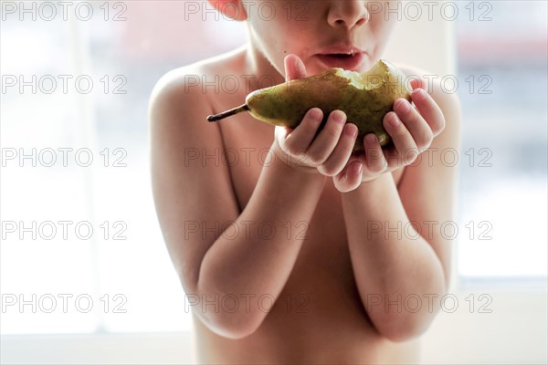 Naked Caucasian boy eating pear