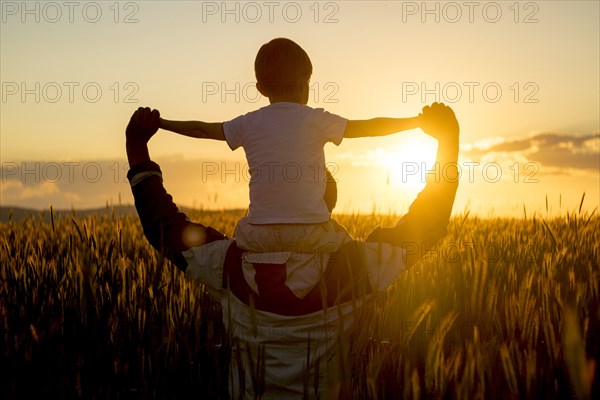 Father carrying son on shoulders in field of wheat at sunset