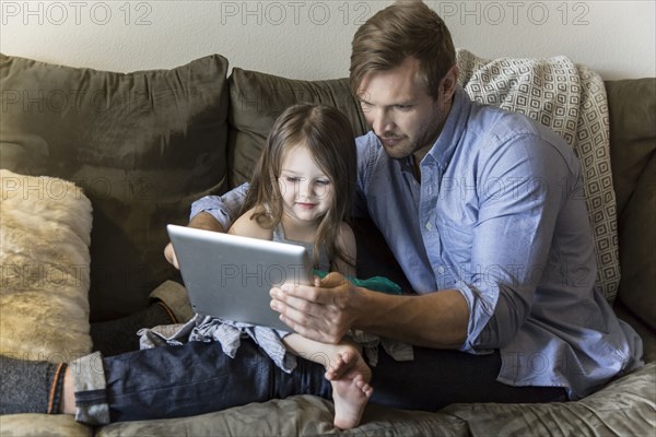 Father and daughter using digital tablet on sofa