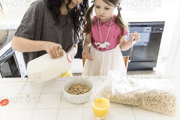 Caucasian mother and daughter eating cereal in kitchen