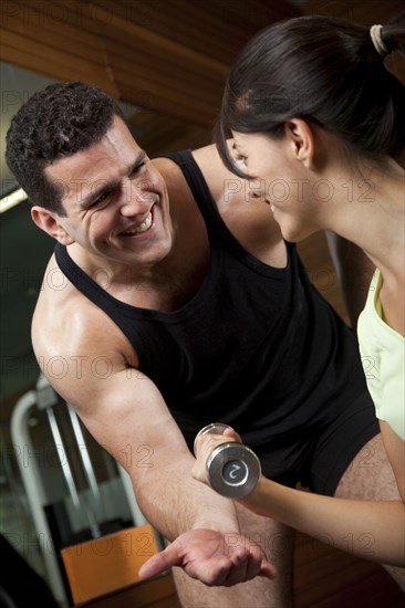 Middle Eastern man helping woman lift weights