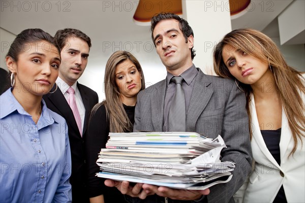 Frustrated Hispanic business people with pile of paperwork