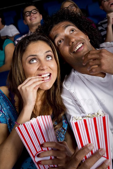 Hispanic couple enjoying popcorn in movie theater