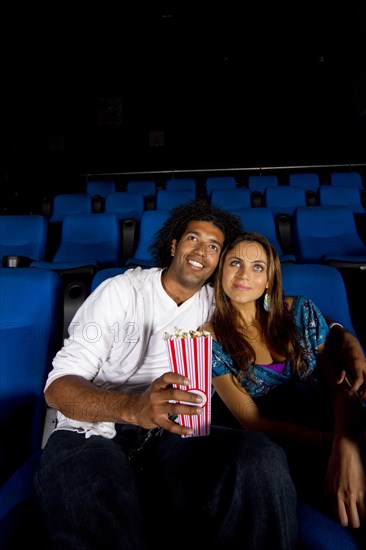 Hispanic couple enjoying popcorn in movie theater