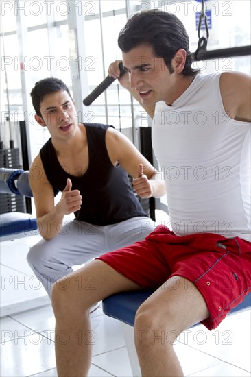 Hispanic man working with personal trainer in health club