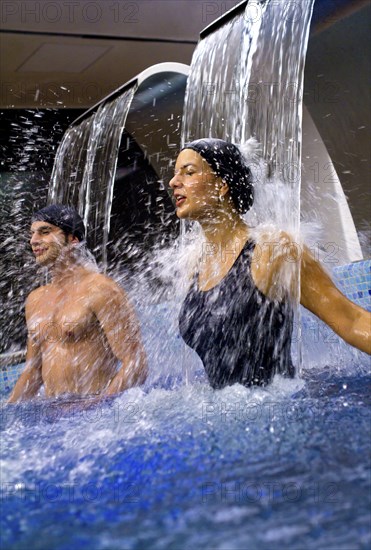 Hispanic couple enjoying waterfall in swimming pool