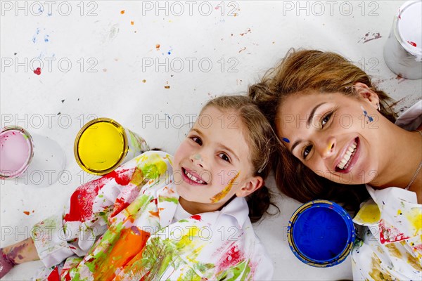 Hispanic mother and daughter covered in paint laying on floor