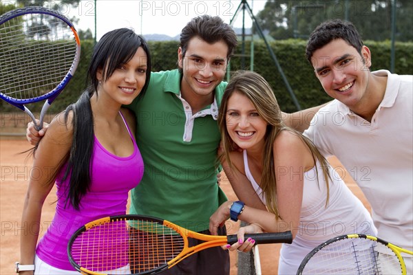Hispanic couples smiling near tennis court net