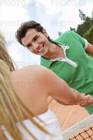 Hispanic couple shaking hands over tennis court net