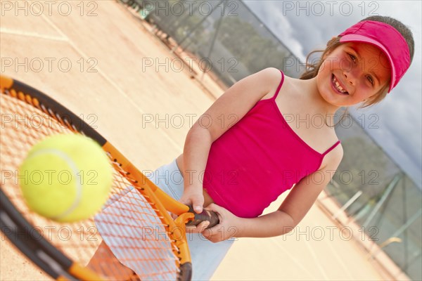 Hispanic girl balancing tennis ball on racquet