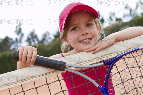 Hispanic girl leaning on net on tennis court