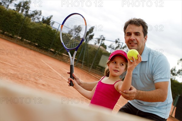 Hispanic man teaching girl to play tennis