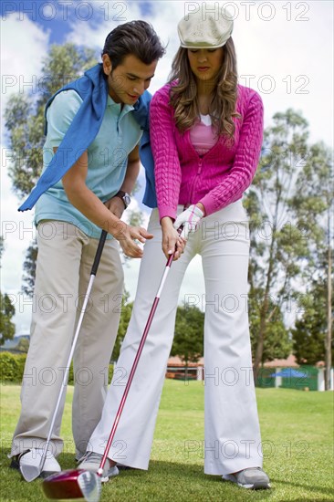 Hispanic man teaching girlfriend to play golf