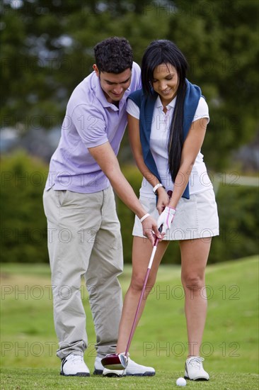 Hispanic man teaching girlfriend to play golf