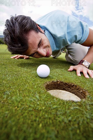 Hispanic man looking at golf ball near cup