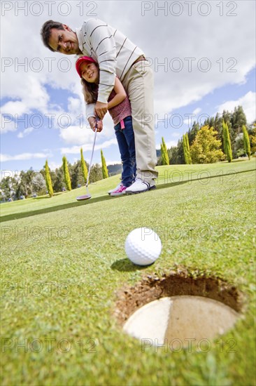 Hispanic man teaching girl to play golf