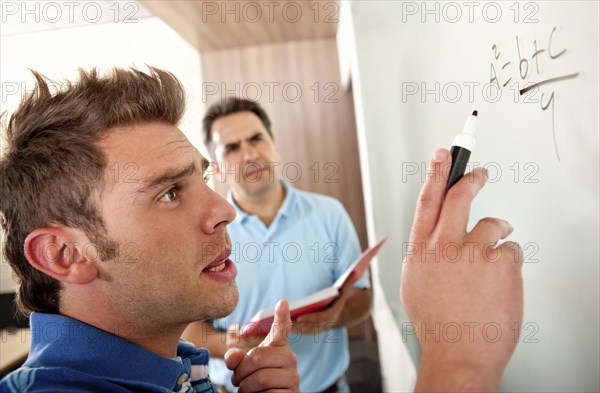 Hispanic teacher watching student writing on whiteboard