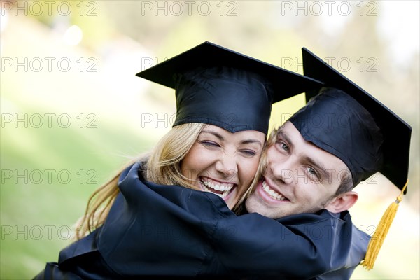 Graduating Hispanic couple in cap and gown hugging