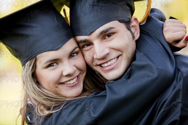 Graduating Hispanic couple in cap and gown hugging