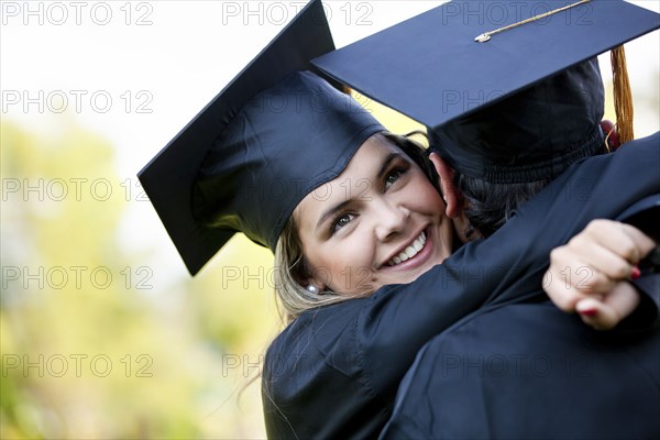 Graduating Hispanic couple in cap and gown hugging