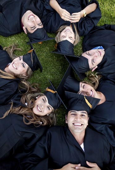 Hispanic graduates in caps and gowns laying in grass