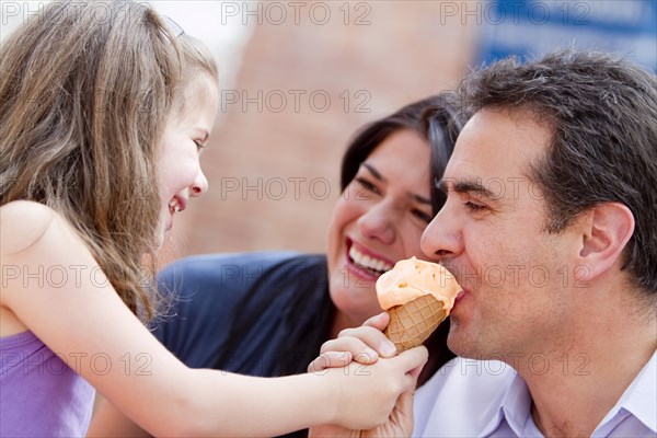 Hispanic girl giving father a bite of her ice cream cone