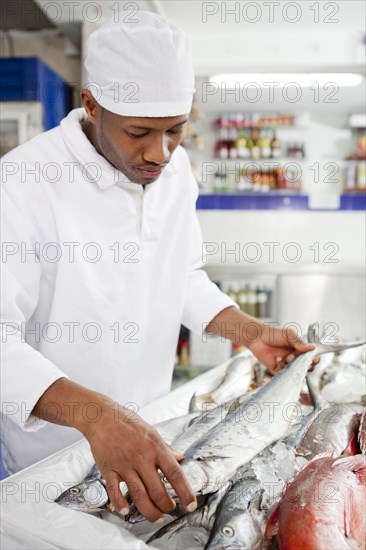 Mixed race grocer preparing fish in market