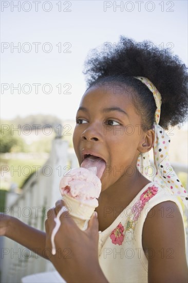Mixed race girl licking melting ice cream cone