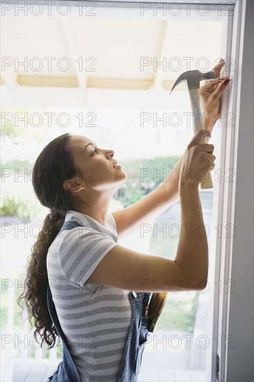 Mixed race woman hammering nail in doorway